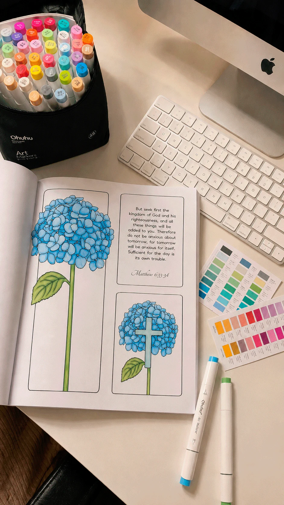 Soulmar coloring book open on a desk with hydrangea pages, markers and a color chart